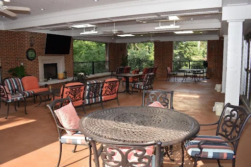 Covered patio with a fireplace, cushioned seating, and tables overlooking the trees